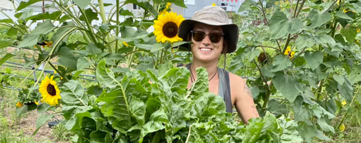 Kamloops Food Policy volunteer wearing sunglasses and a hat holding greens