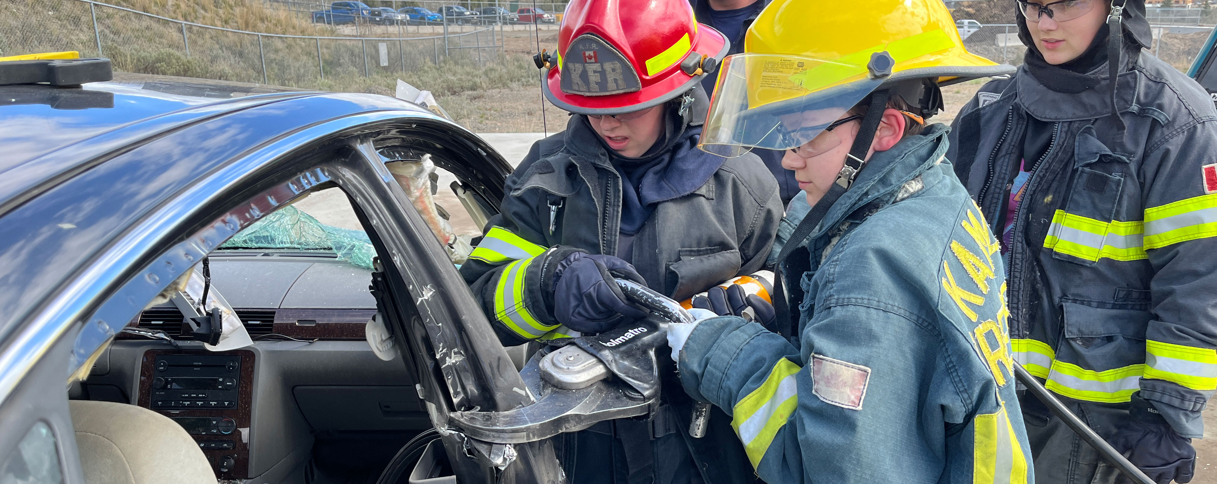two female students in firefighter gear performing a vehicle extraction