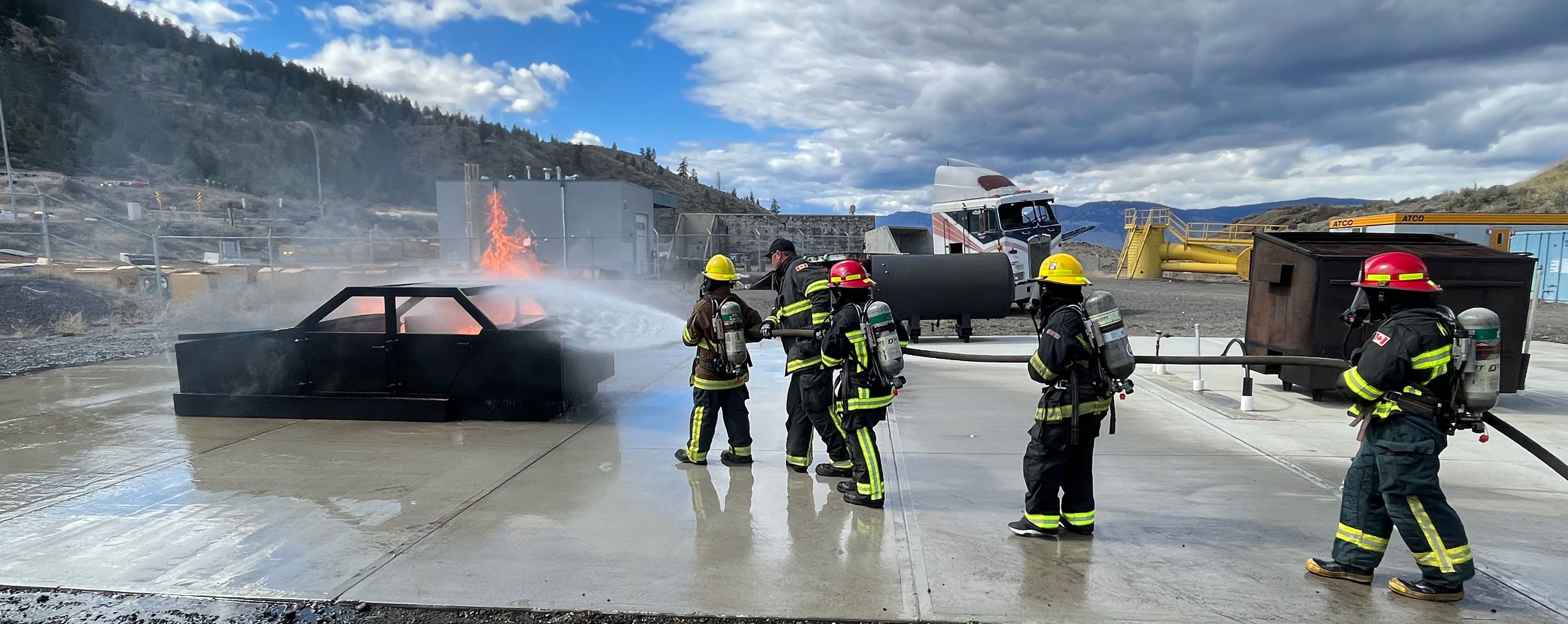 four students in firefighter gear putting out a fire on a training vehicle