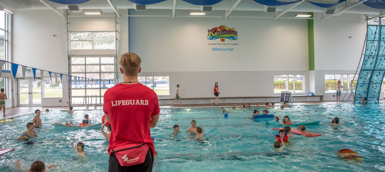 Lifeguard standing on deck of pool with swimmers