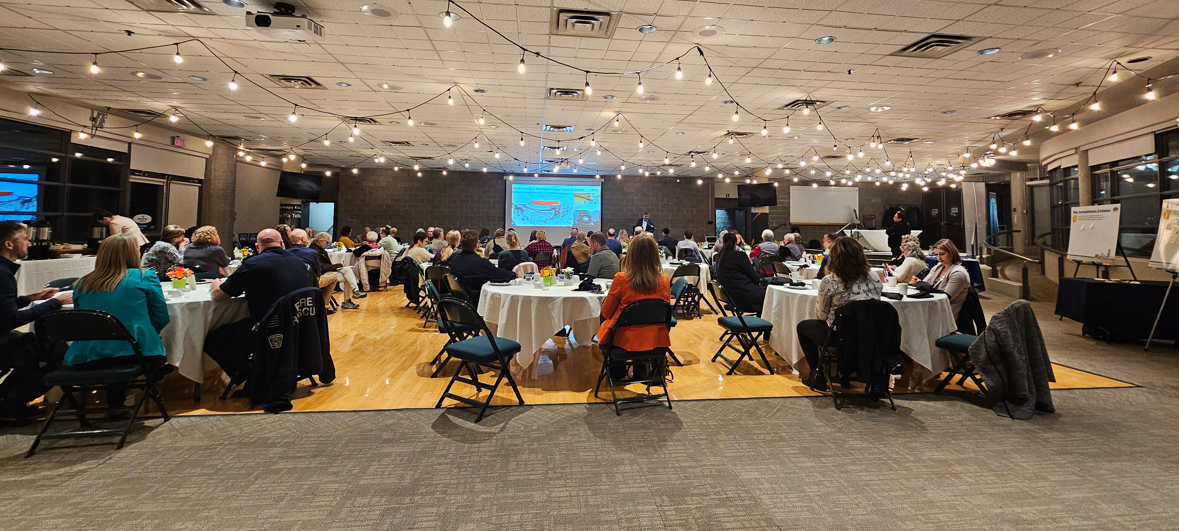 guests in room around tables in front of presentation screen