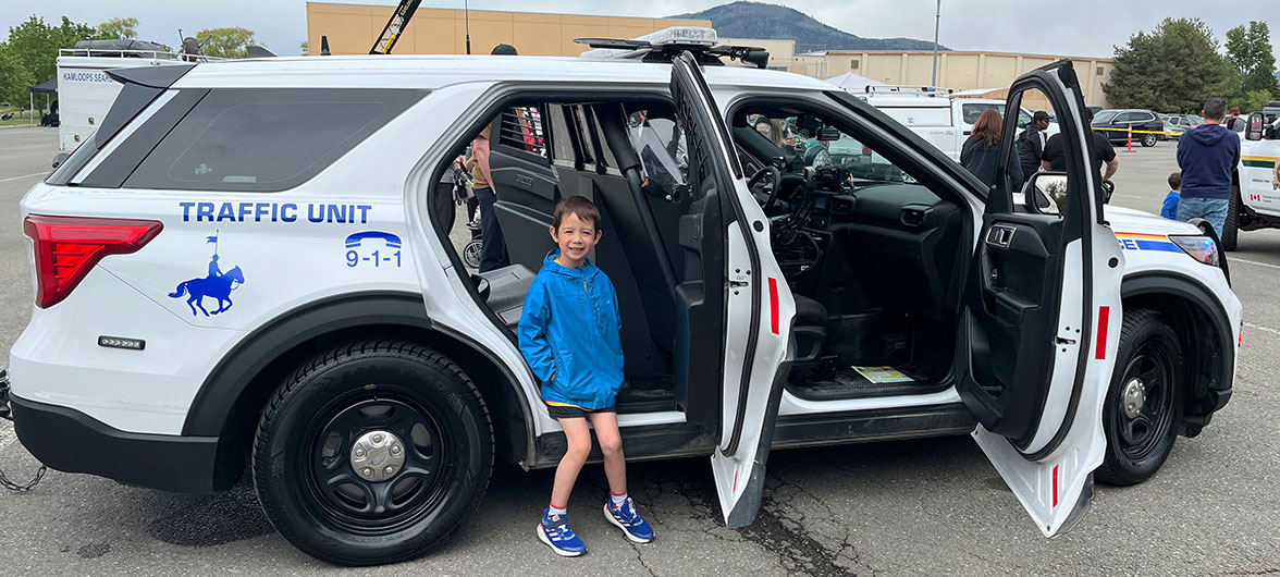 child standing in front of rear door of a police car