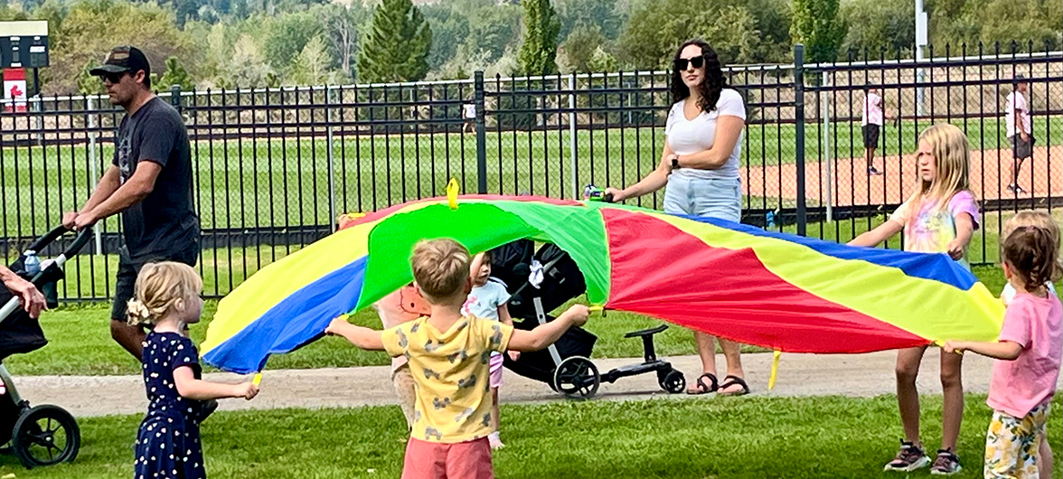 kids puffing up a large round parachute in a park