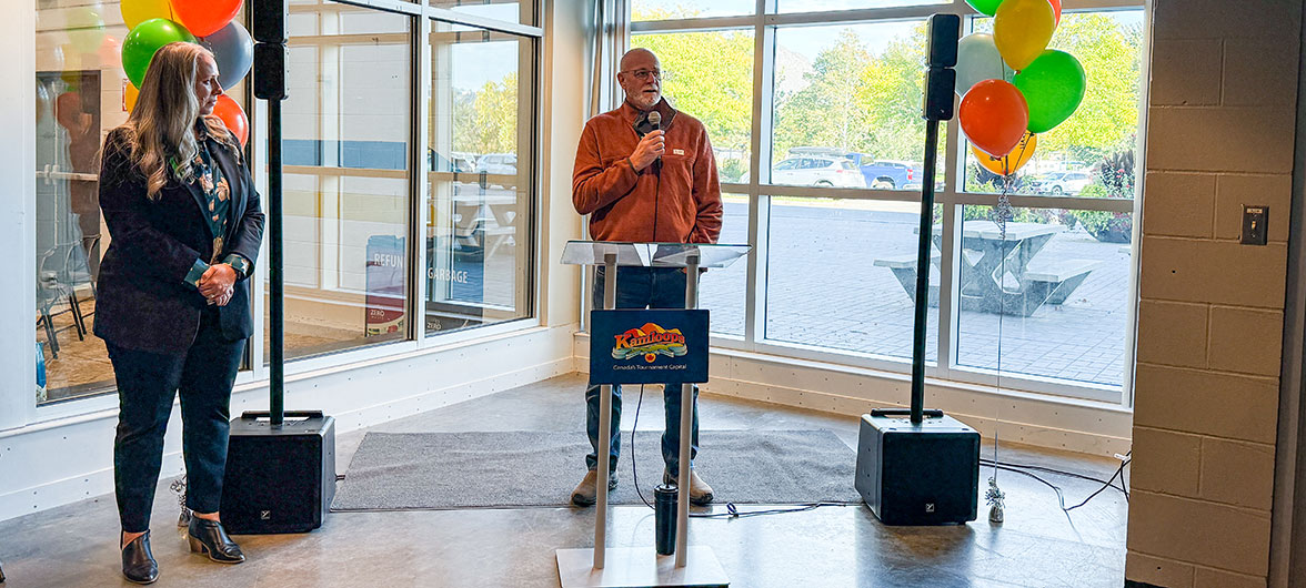 senior man in orange jacket speaking behind a podium