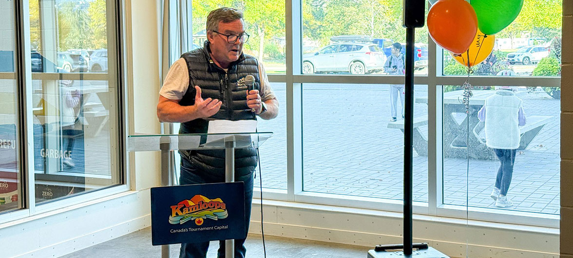 senior man in a dark vest speaking behind a podium