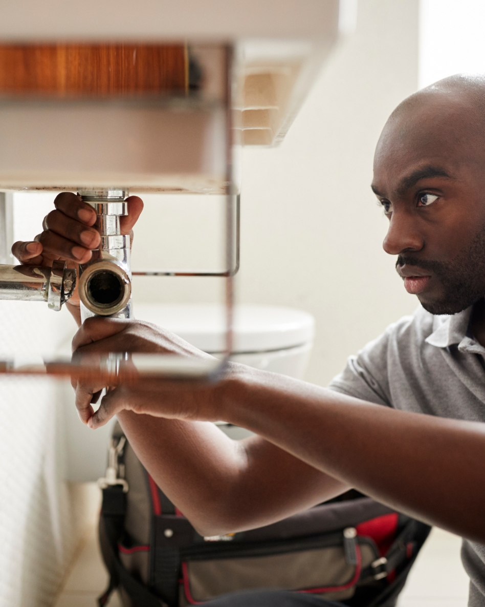 A plumber tightens a pipe underneath a bathroom sink.