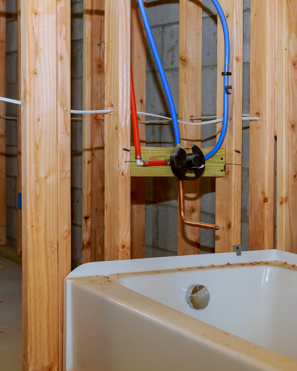 A bathtub in front of exposed plumbing in unfinished framed walls.