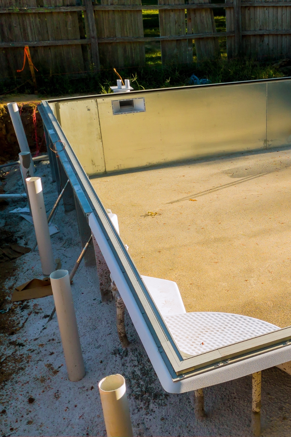 An in-ground swimming pool sits getting installed in a hole in a yard.
