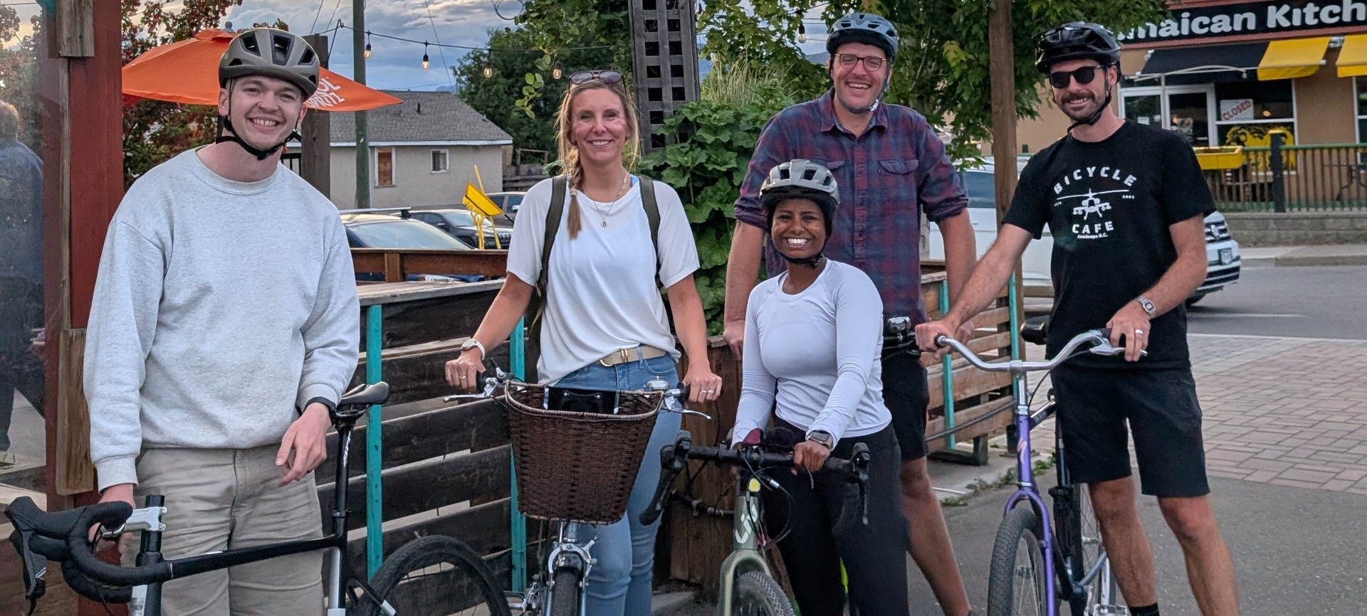 Five diverse cyclists standing with their bikes smiling at the camera outside Red Beard Cafe