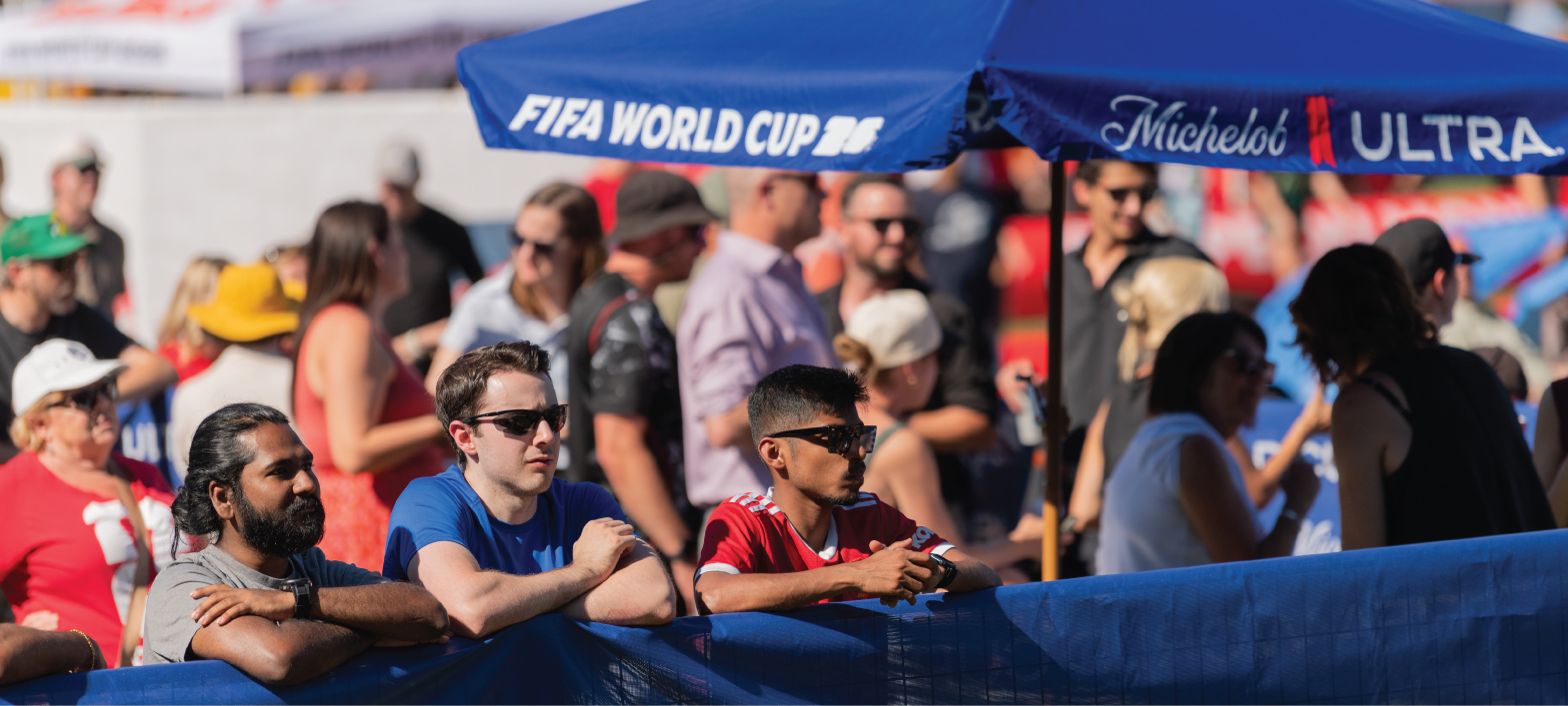 a big crowd of spectators in a beer garden in Riverside Park watching a soccer match on a big screen