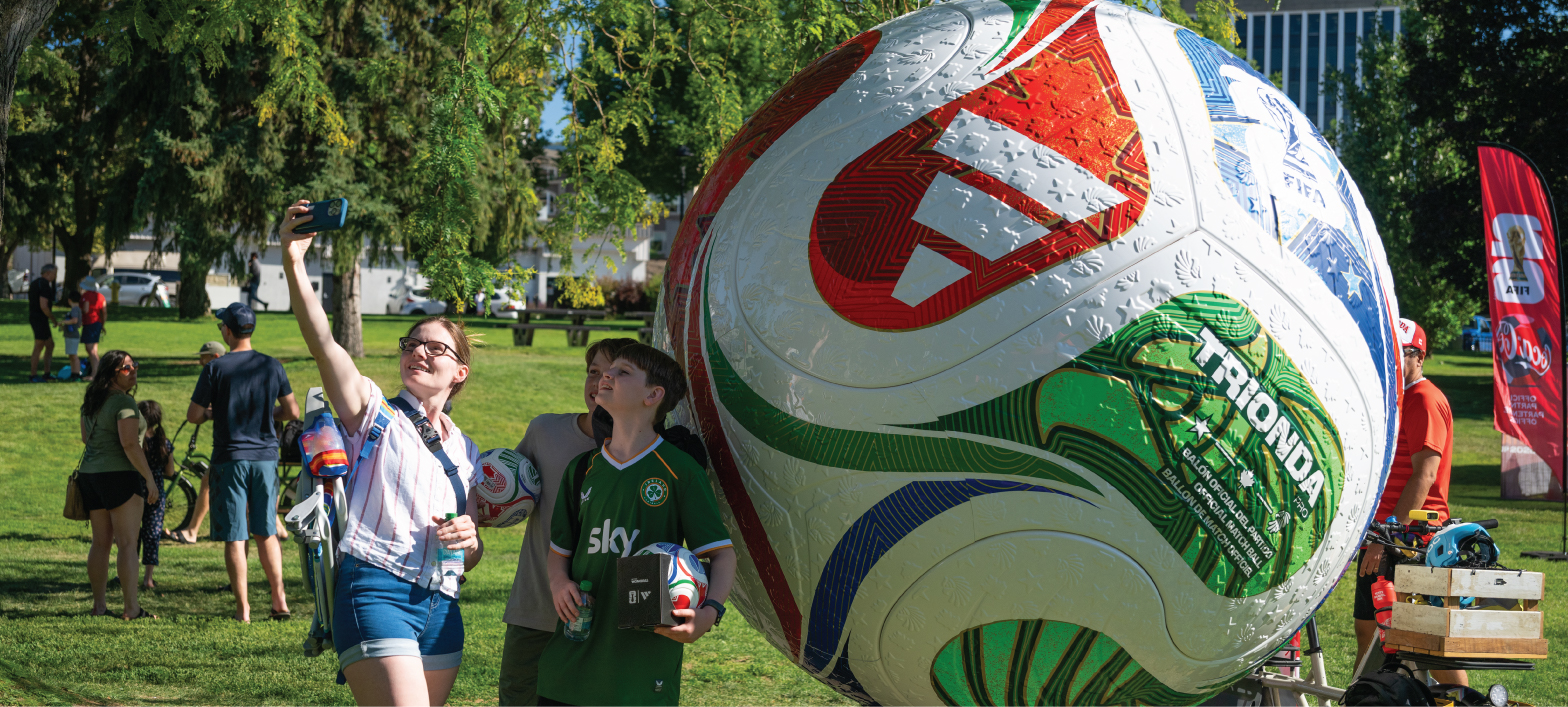 a couple of soccer fans taking a selfie in front of a giant soccer ball set up in Riverside Park