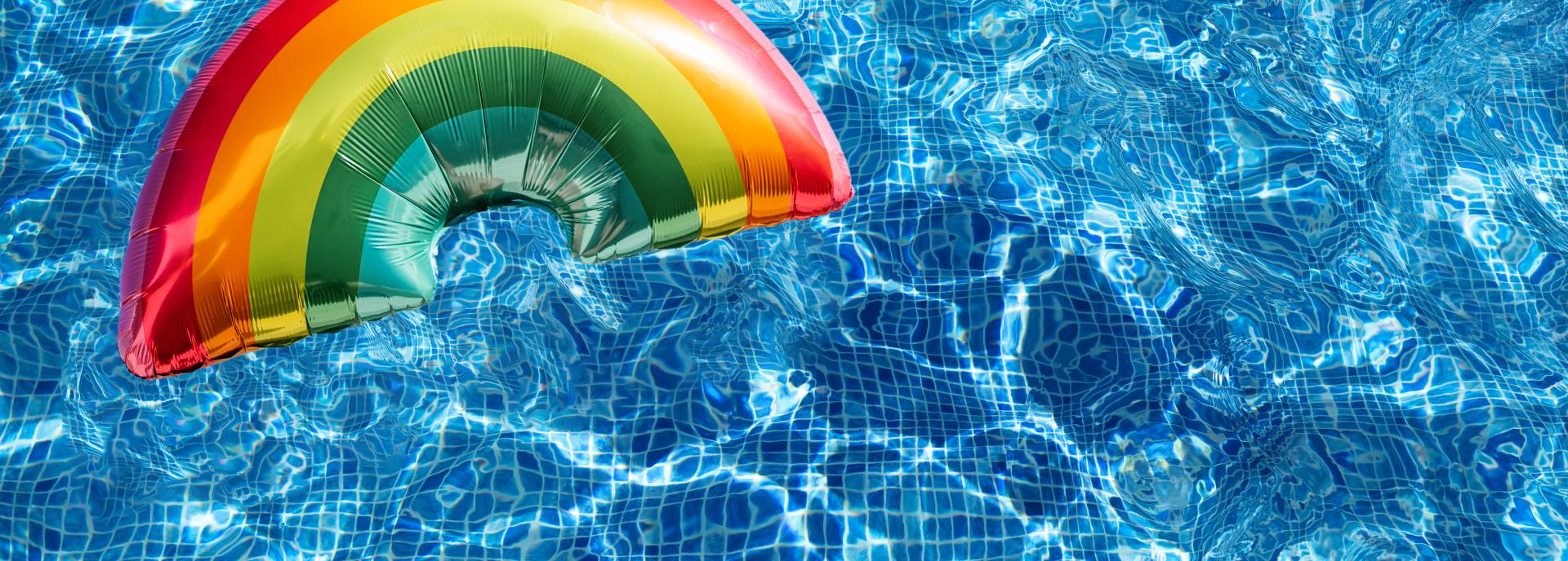 Clear blue pool water with a large rainbow shaped balloon floating